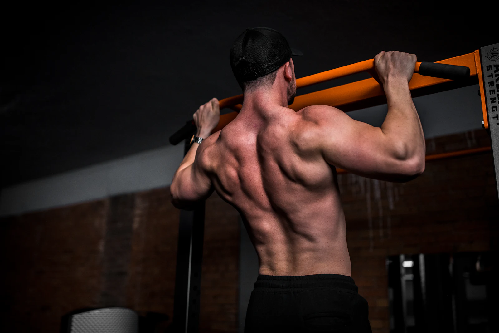 Athlete gripping a pull-up bar, back muscles lit from above